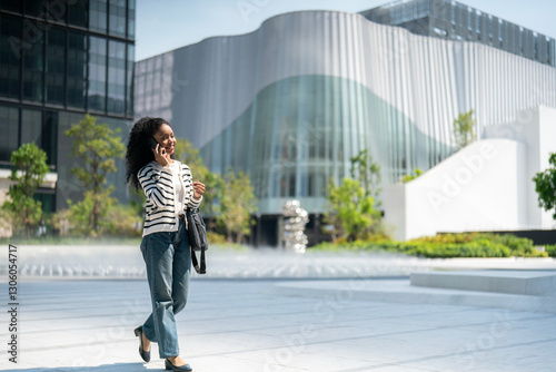 Confident young woman talking on phone while walking in the city, urban professional communication.