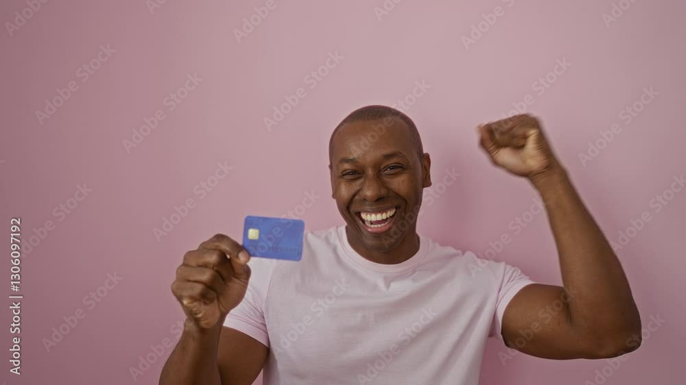 Man smiling holding credit card in front of pink background showcasing excitement and celebration in an isolated setting