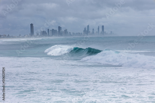 A large windswept wave, part of the effects of the edge of cyclone Alfred off the Queensland coast, breaks with Surfers Paradise in the background under threatening skies on the Gold Coast, Australia. photo