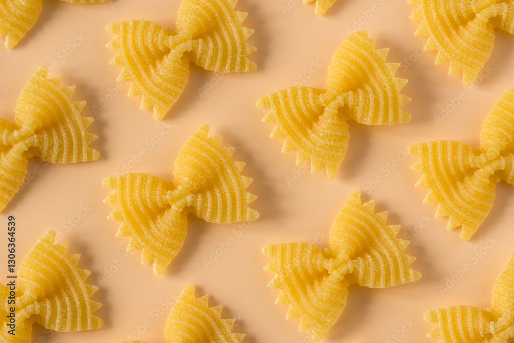 Background of raw pasta . Top view isolated of a raw italian durum wheat farfalle pasta against a light orange background .