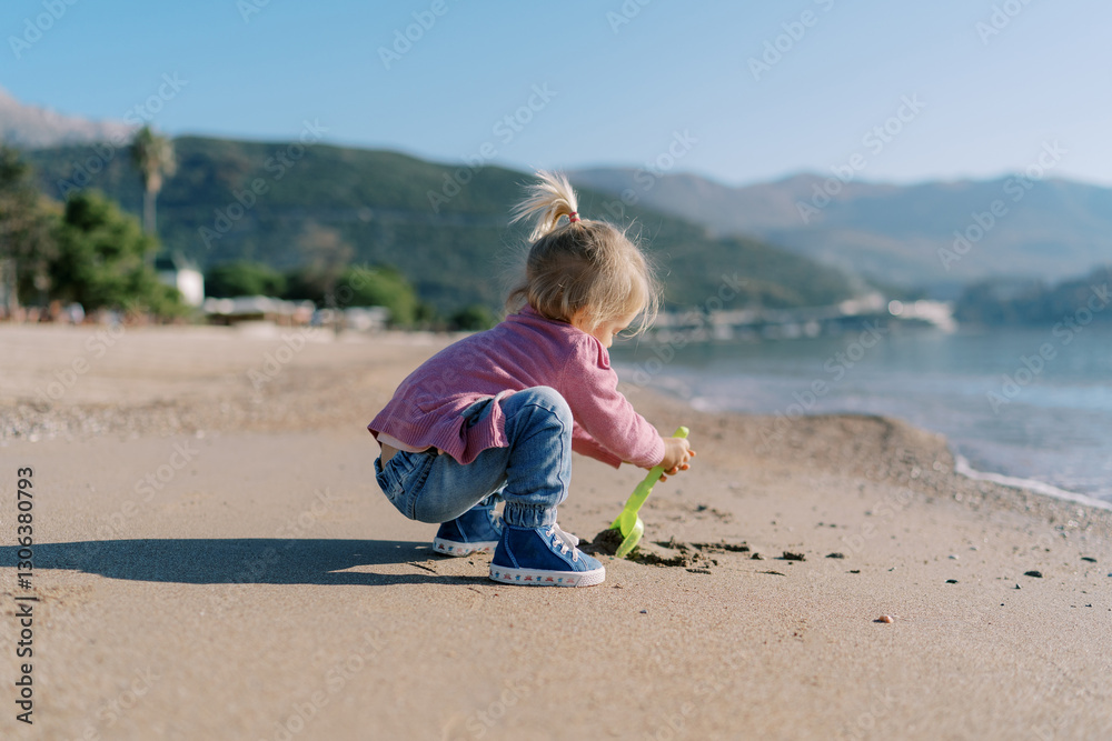 Little girl digs sand on the beach with a toy shovel. Side view Little girl digs sand on the beach with a toy shovel. Side view