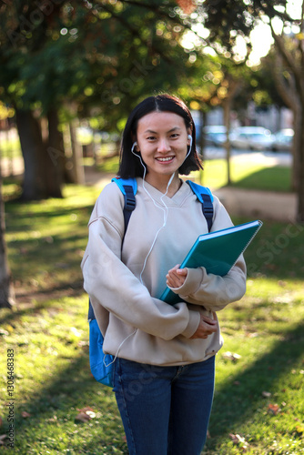 Smiling young asian student with backpack and notebook outdoors