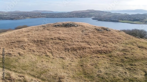 A grassy hill overlooking a calm blue sea and a distant town