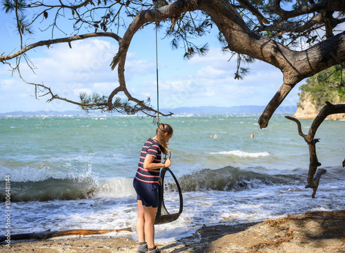 Obraz na płótnie Woman checking the tyre swing on the beach. Unrecognizable people swing at Kendall Bay. Kauri Point Centennial Loop track. Auckland. w salonie
