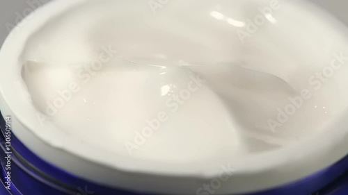 A moisturizing cream is being scooped from its container, showcasing a smooth and creamy texture ideal for skincare application.
