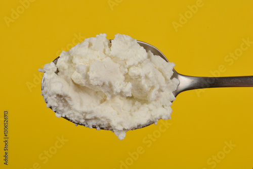 A close-up shot of a spoonful of creamy white cottage cheese against a yellow background, showcasing its lumpy texture photo