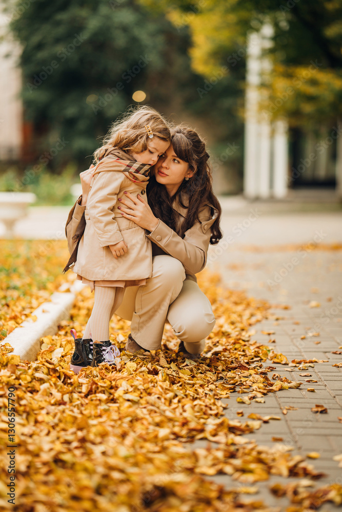 Mother and daughter enjoying autumn in a park filled with fallen leaves