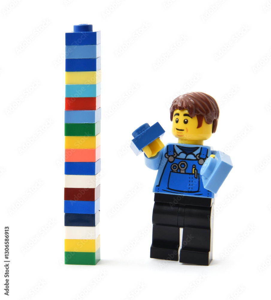 Fototapeta premium Lego minifigure is building a tall brick tower from colorful blocks. Editorial illustrative image of popular plastic toy constructor.