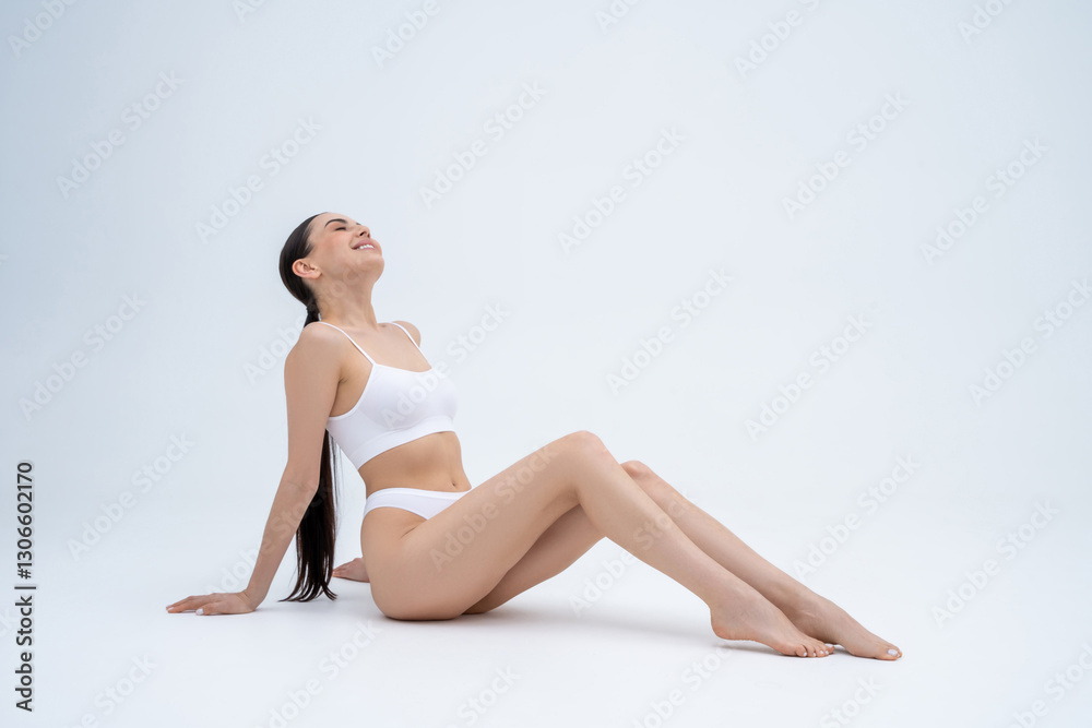 Sweet long-haired slim woman in white lingerie sitting on floor and smiling nicely Sweet long-haired slim woman in white lingerie sitting on floor and smiling nicely