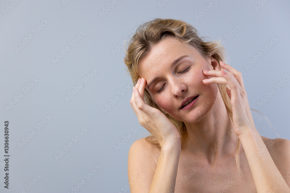 Fototapeta premium Woman with Light Hair Using Hands to Ease Stress on the Face in a Relaxed Expression Against a Soft Gray Background, Emphasizing Comfort and Serenity in a Calm Setting