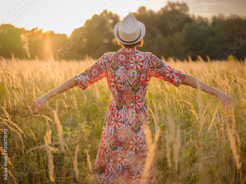 Young woman walking through picturesque European field in late summer. Golden sunlight, lush greenery, and serene rural atmosphere create peaceful countryside scene.