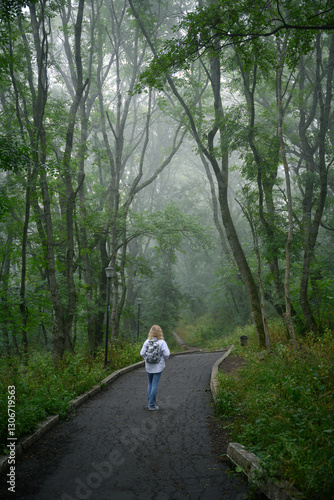 Obraz na płótnie Woman walking on forest path with tall trees in misty green woods on foggy morning w salonie