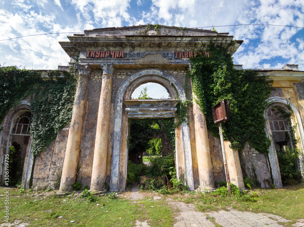 Obraz premium Main gates of railway station in abandoned Tkvarcheli city, Abkhazia. Old building ruins overgrown by grass in summer. Concept of war, grunge, architecture