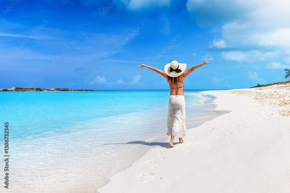 A happy woman with a sunhat walks down a tropical paradise beach in the Caribbean islands, Bahamas