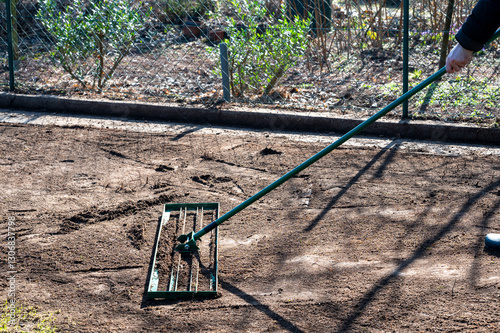 Man uses a lawn rake to level the ground in the garden to even out any unevenness and prepare the ground for a perfect lawn.