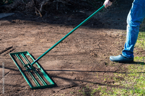 Man uses a lawn rake to level the ground in the garden to even out any unevenness and prepare the ground for a perfect lawn.