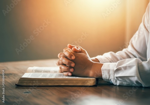 Praying hands resting on open bible, warm sunlight illuminating wooden surface, expressing spiritual reflection and deep religious connection