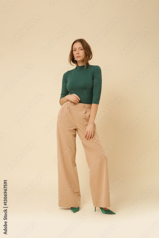 Obraz premium Series of studio photos of young female model wearing simple beautiful outfit, green turtleneck top and beige wide leg trousers
