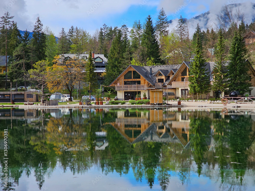 Wooden hotel reflecting on calm jasna lake waters, framed by lush greenery and julian alps in scenic kranjska gora, slovenia Wooden hotel reflecting on calm jasna lake waters, framed by lush greenery and julian alps in scenic kranjska gora, slovenia