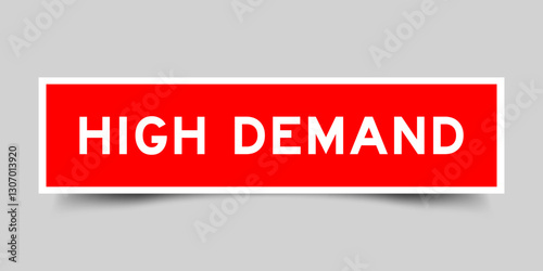 Red color square shape sticker label with word high demand on gray background