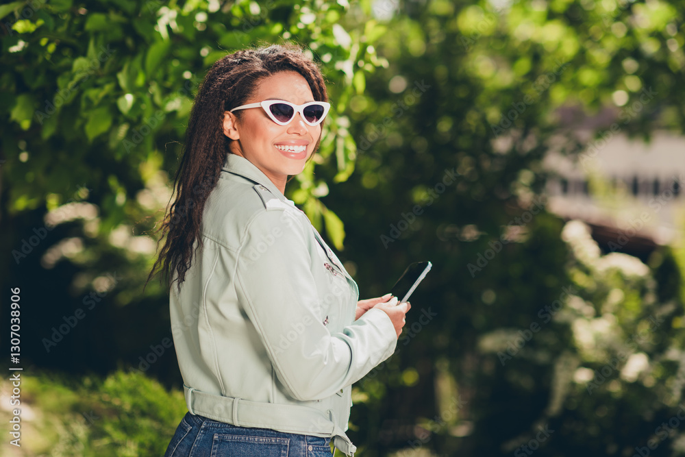 Young woman enjoying sunny day outdoors in casual style, wearing stylish coat and sunglasses, holding smartphone. Young woman enjoying sunny day outdoors in casual style, wearing stylish coat and sunglasses, holding smartphone.