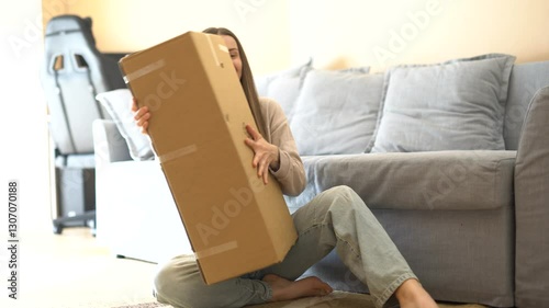 Happy young woman sitting on the floor with a big package. She smiles, shakes the box, and enjoys the excitement of unboxing. Perfect for delivery, online shopping, and surprise themes!