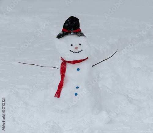 A large snowman wearing a red scarf, and tp hat, with buttons, stands in a snow covered yard.
