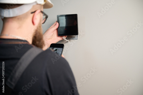 Security alarm installation. Security technician installing safe monitor on wall in the new office. Installing security system. Man worker installing alarm technology insurance in home