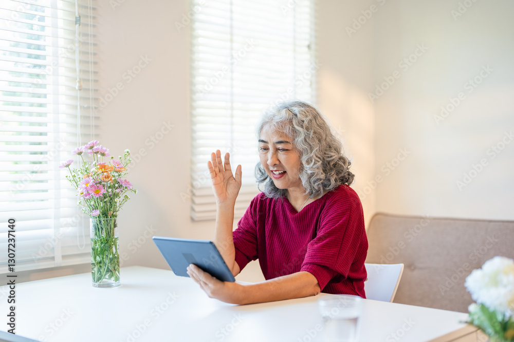 60s older mature middle aged adult woman waving hand holding digital tablet computer video conference calling family or Friend online chat meeting sitting on couch at home.