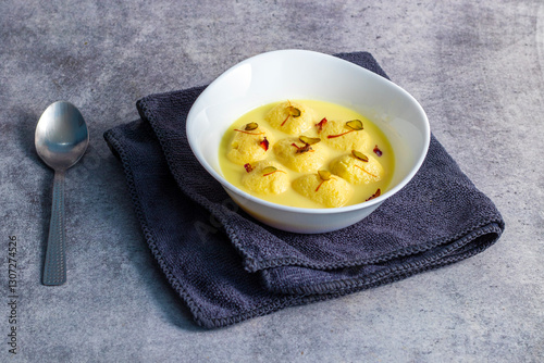 Rasmalai is a soft, spongy Indian dessert made of chhena (paneer) dumplings soaked in sweet, flavored milk, garnished with saffron, cardamom, and nuts. photo