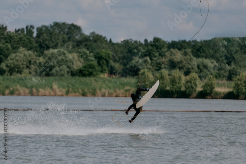 A man on a wakeboard on a lake falls during an unsuccessful stunt in the air against a background of trees, on a summer day