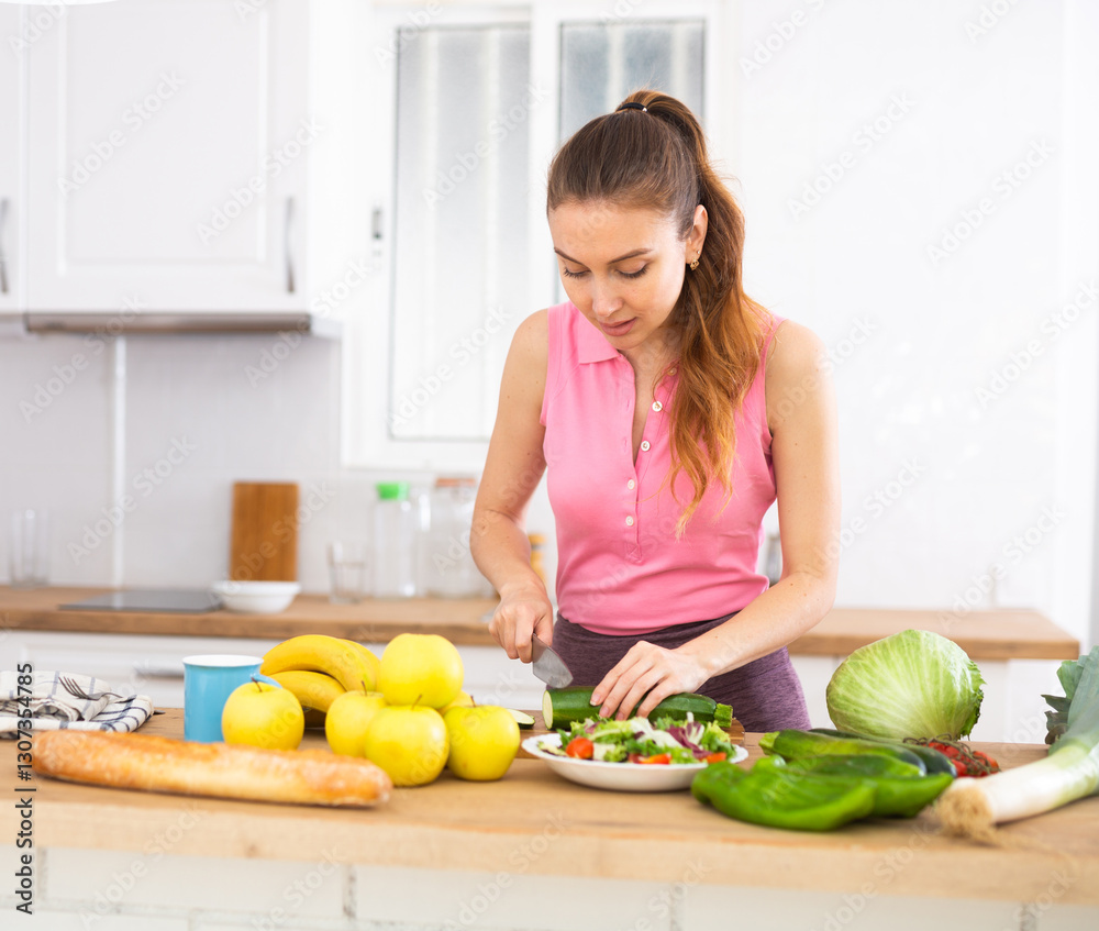 Smiling young woman preparing vegetable salad in home kitchen Smiling young woman preparing vegetable salad in home kitchen