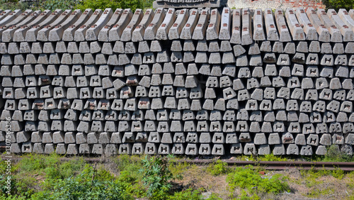 Stacked concrete railway sleepers arranged in a large pile. Each sleeper has a rectangular shape with internal metal reinforcements visible at the ends, creating patterned cutouts.