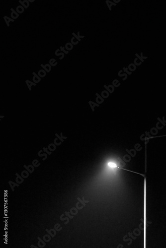 A solitary street lamp emits a bright white light, cutting through the darkness of the night.