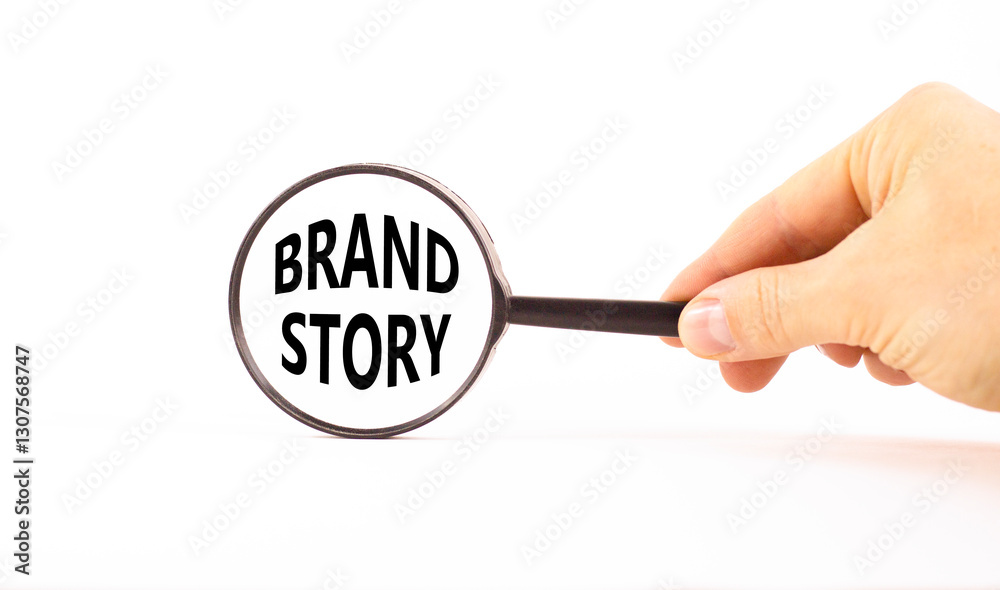 Brand story branding symbol. Concept words Brand story on beautiful white paper in magnifying glass. Businessman hand. Beautiful white background. Business brand story branding concept. Copy space. Brand story branding symbol. Concept words Brand story on beautiful white paper in magnifying glass. Businessman hand. Beautiful white background. Business brand story branding concept. Copy space.