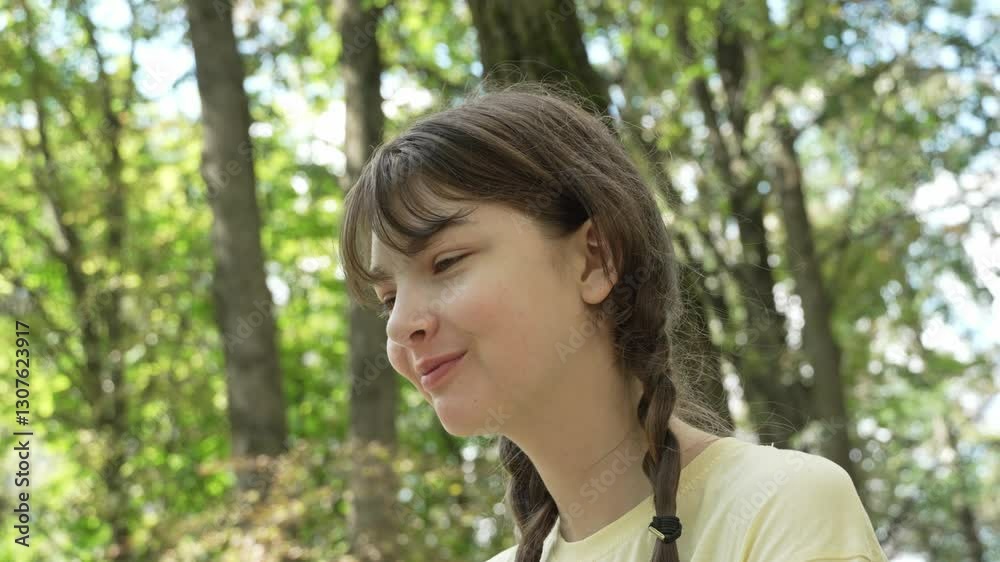 A teenage girl with pigtails in a yellow t-shirt smiles sweetly and wipes her hands with a wet napkin after lunch in a city park on a sunny summer day. Left-side shot, close-up A teenage girl with pigtails in a yellow t-shirt smiles sweetly and wipes her hands with a wet napkin after lunch in a city park on a sunny summer day. Left-side shot, close-up