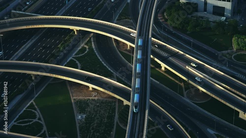 Dubai metro train drive on elevated tracks over highway junction interchange amidst the modern cityscape of Dubai downtown at sunset, no logos