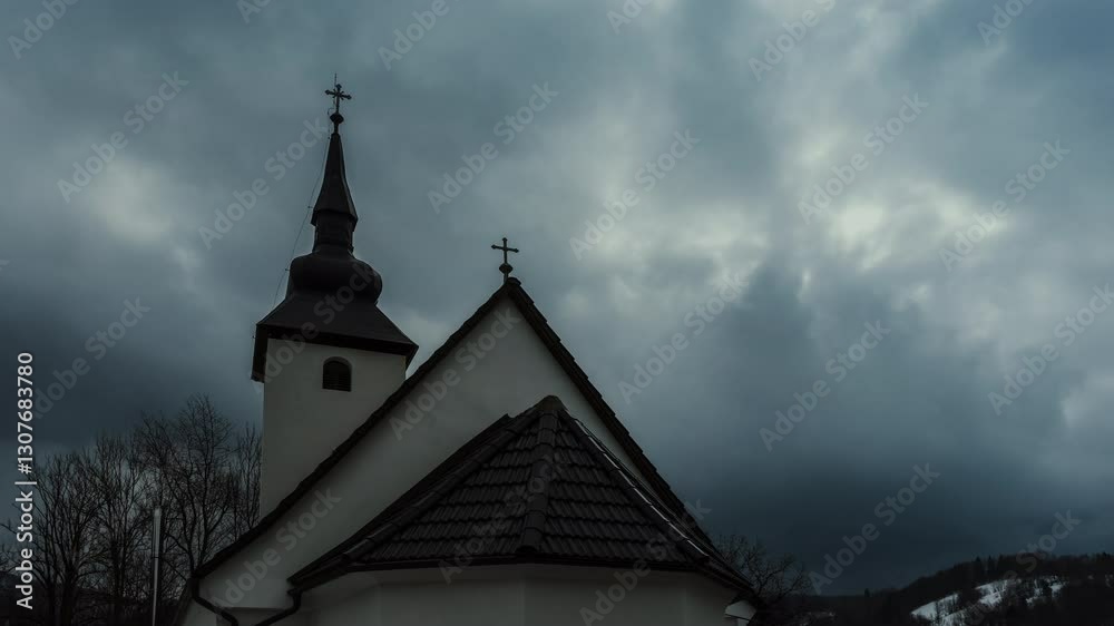 A small chapel with a dark tiled roof and elegant steeple sits against a dramatic cloudy sky. The peaceful setting and religious symbols create an atmosphere of reflection, devotion and reverence A small chapel with a dark tiled roof and elegant steeple sits against a dramatic cloudy sky. The peaceful setting and religious symbols create an atmosphere of reflection, devotion and reverence