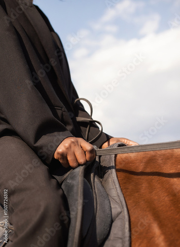 girl in black suit sitting on horse, close-up of hands holding horse