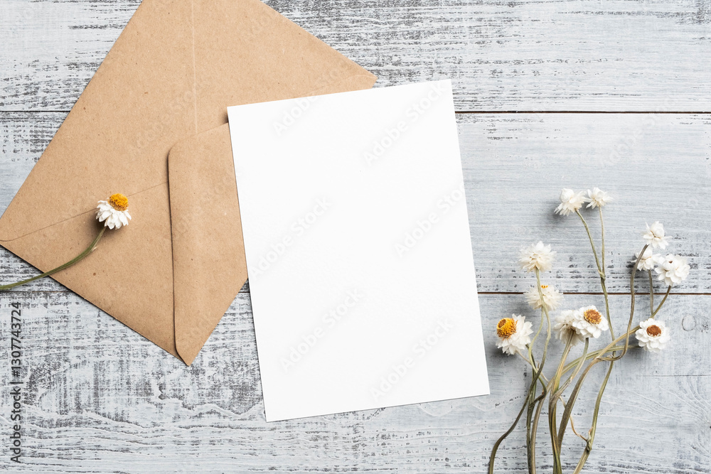 Fototapeta premium Blank wedding invitation card mockup with craft envelope and dried flowers decor, copy space for card design, flat lay on wooden background