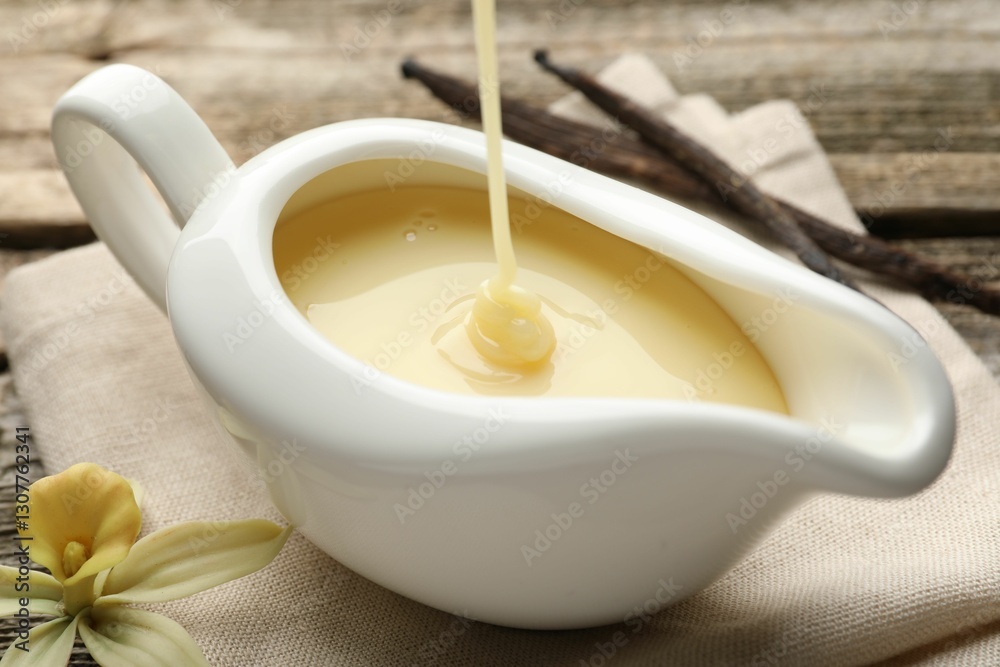 Pouring tasty vanilla condensed milk into gravy boat on wooden table, closeup Pouring tasty vanilla condensed milk into gravy boat on wooden table, closeup