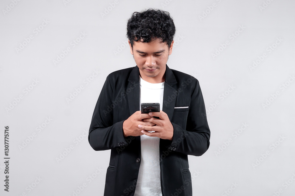 Asian man in black blazer and white t-shirt holding a smartphone with a friendly smile. Isolated on gray background. Concept of communication, technology, and business. Asian man in black blazer and white t-shirt holding a smartphone with a friendly smile. Isolated on gray background. Concept of communication, technology, and business.