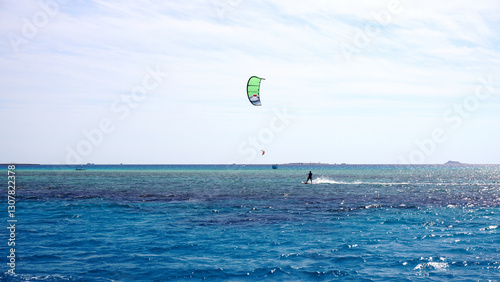 A kitesurfer is soaring above the clear waters of the Red Sea on a sunny summer day. With a bright blue sky and turquoise sea, this scene is perfect for travel, adventure, and watersports content. 