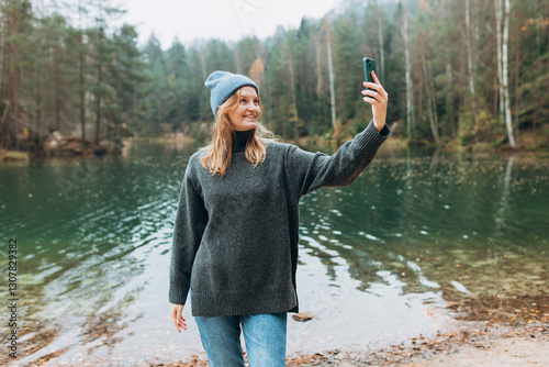 Happy blonde Woman makes selfie mobile photo enjoying mountain lake landscape. Nature freedom adventure, vacation video call, girl tourist outdoors. Concept of an active lifestyle