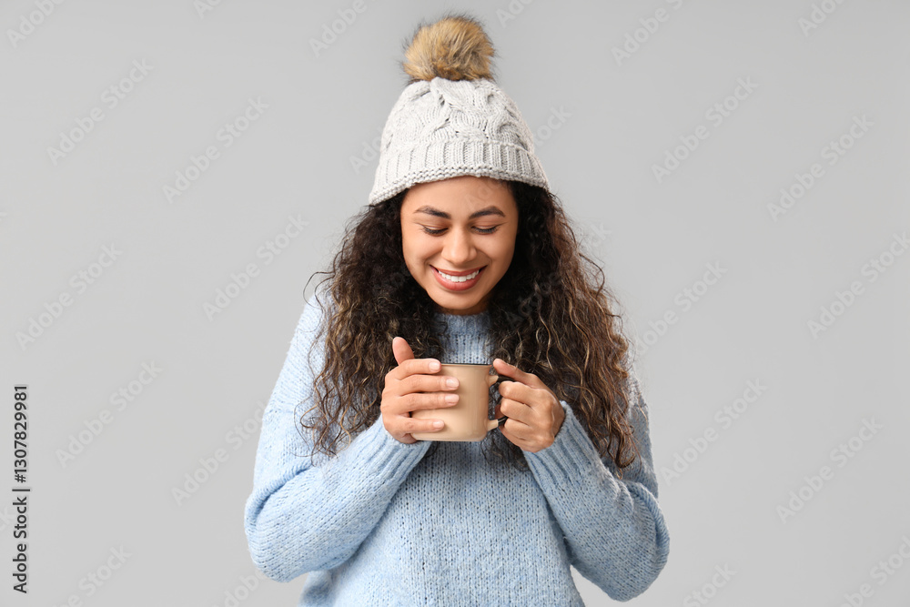 Beautiful young African-American woman with cup of hot mulled wine on grey background Beautiful young African-American woman with cup of hot mulled wine on grey background