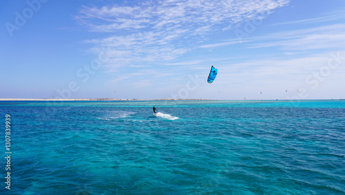 A kitesurfer above the clear waters of the Red Sea on a sunny summer day. With a bright blue sky and turquoise sea, this scene is perfect for travel, adventure, and watersports content