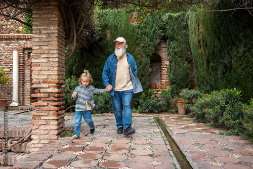 Εκτύπωση καμβά A grandfather and his grandson hold hands as they walk through a serene garden,