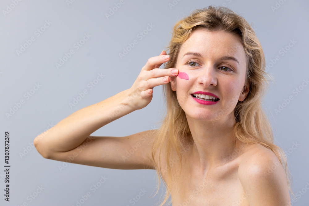 Beauty Routine: Young Woman Applying Skincare on Her Face with a Pink Cream Delightfully Smiling in a Minimalist Setting Beauty Routine: Young Woman Applying Skincare on Her Face with a Pink Cream Delightfully Smiling in a Minimalist Setting