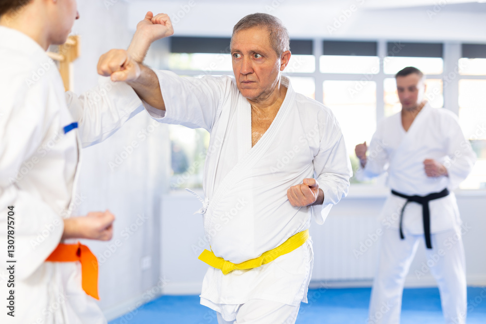 Obraz premium Elderly man and young man in kimono practicing karate techniques in gym