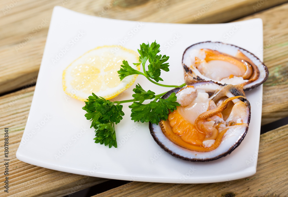 Image of salad of raw dog cockle with lemon and fresh greens at plate